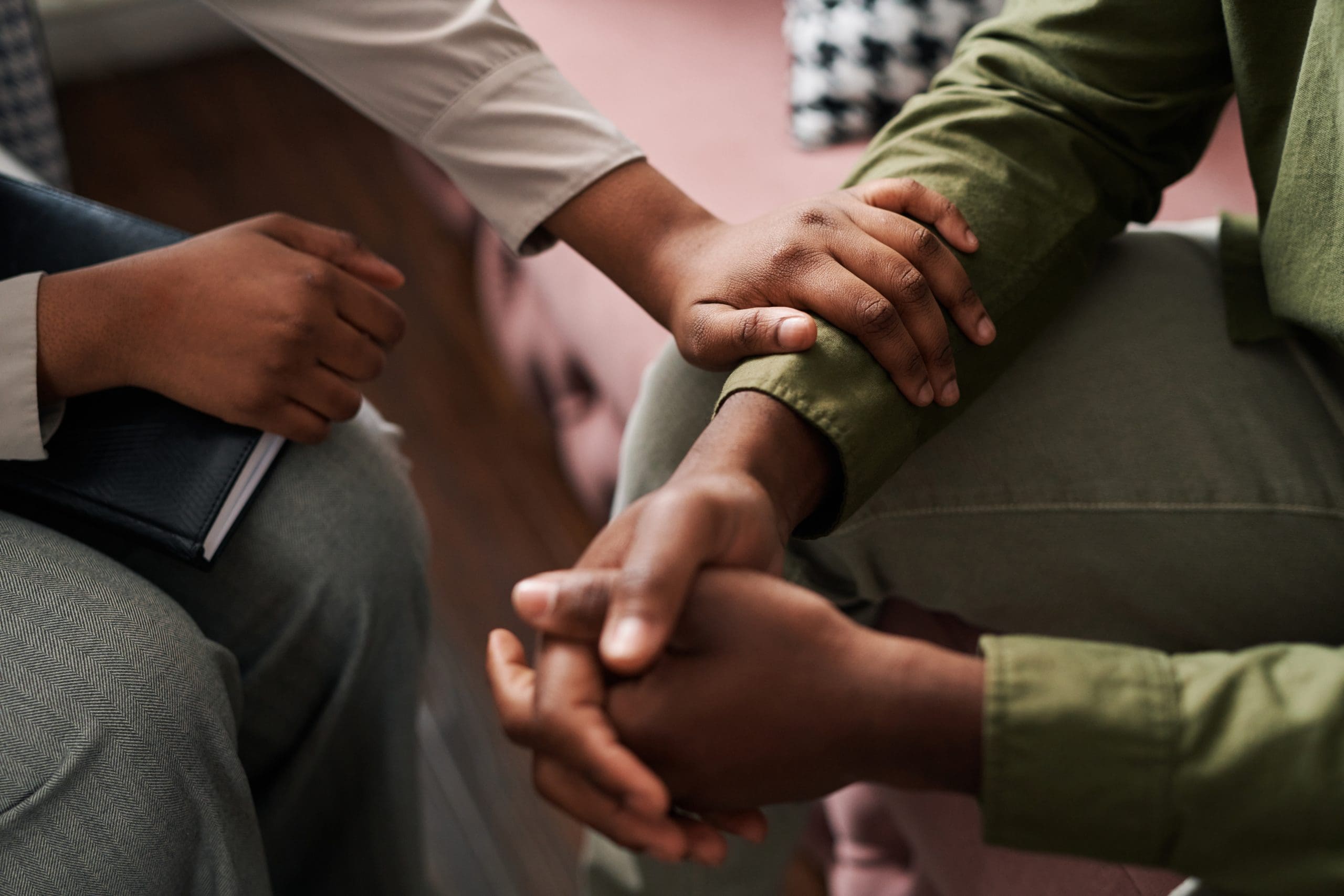 Young African American female psychologist keeping hand of wrist of male patient